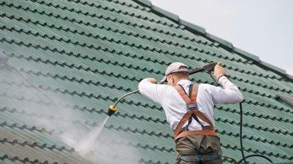 Mitarbeiter reinigt mit dem Hochdruckreiniger ein grün bewachsenes Ziegeldach