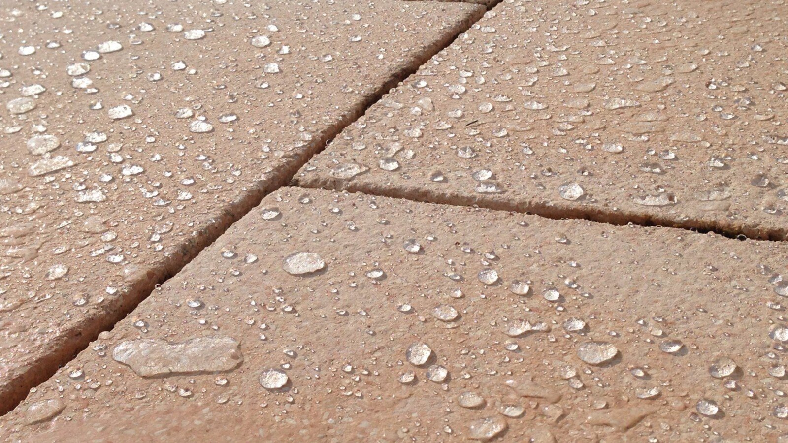 Wassertropfen perlen auf einer imprägnierten, rötlich-beigen Steinoberfläche ab Wassertropfen perlen auf einer imprägnierten, rötlich-beigen Steinoberfläche ab