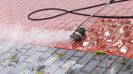 Heisswassergerät entfernt Unkraut aus den Fugen einer roten Pflasterfläche