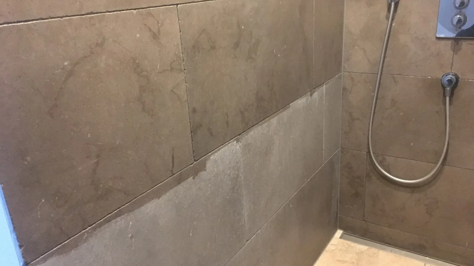 Natursteinfliesen in einer Dusche, teilweise von Kalkflecken befreit
