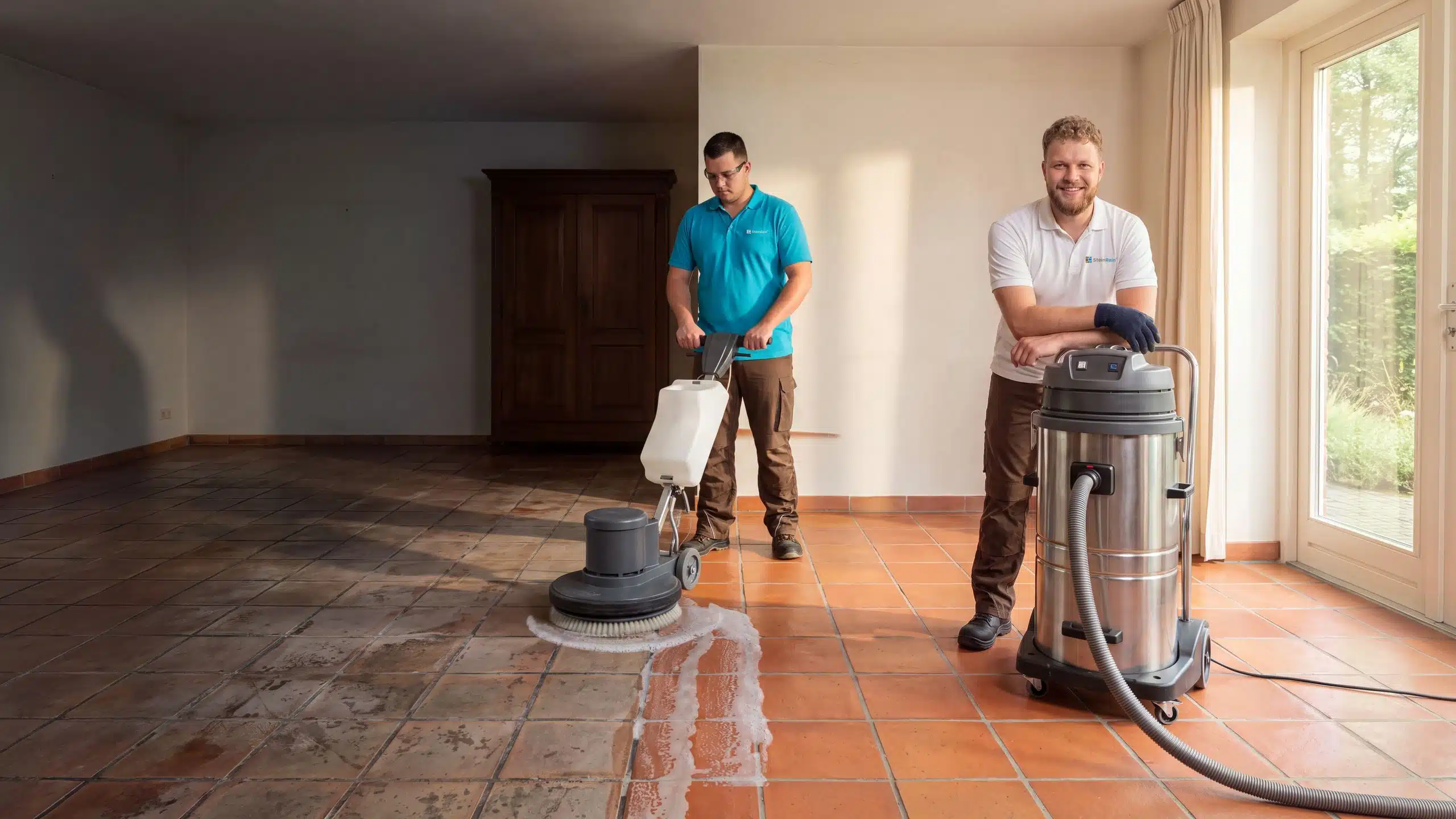 Symbolbild: Cottoreinigung – ein SteinRein-Techniker reinigt einen verschmutzten Terracotta-Boden mit der Einscheibenmaschine, Reinigungsschaum auf den Fliesen, links stumpfe Fliesen mit fast schwarzen Fugen, rechts gereinigter Cotto in satter Farbe mit hellgrauen Fugen, vorn ein Kundenberater im weißen SteinRein-Polo am Industriesauger.